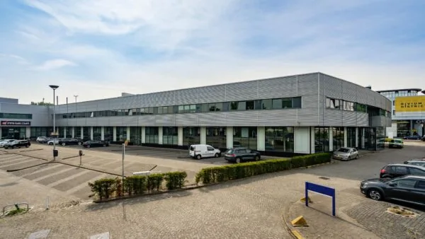 Grijs kantoorgebouw aan de Rivium Boulevard met parkeerplaatsen en diverse geparkeerde auto's.